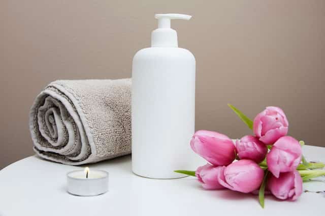 Rolled spa towel beside lotion and flowers