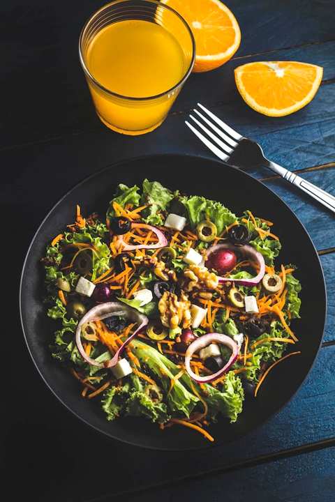 Fresh salad with orange juice and orange slices on a dark table