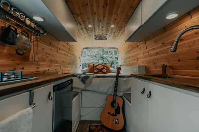 Wood-lined camper van interior with bed, sink, and storage cabinets