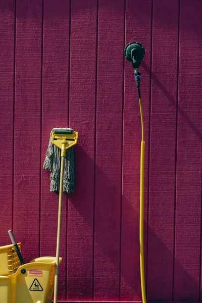Mop, bucket, and cleaning tools against a painted wall